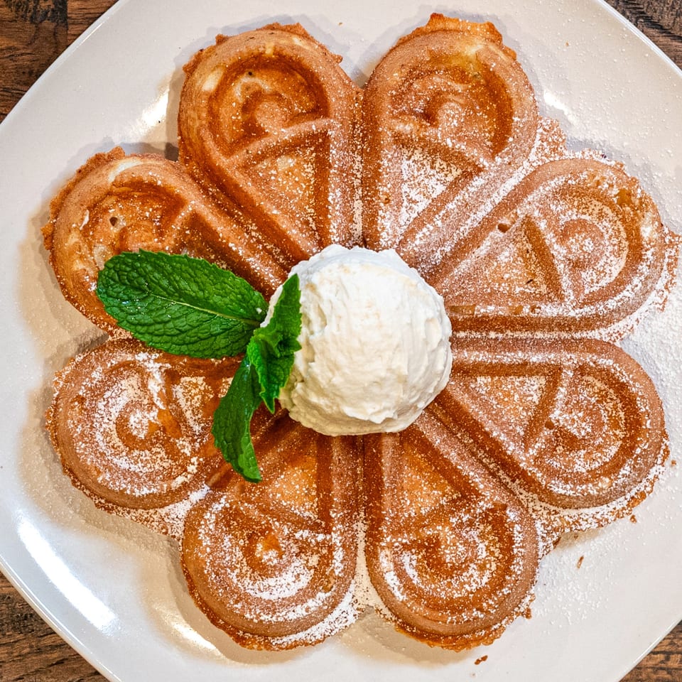 A flower-shaped waffle with powdered sugar, a scoop of ice cream, and mint on a white plate.