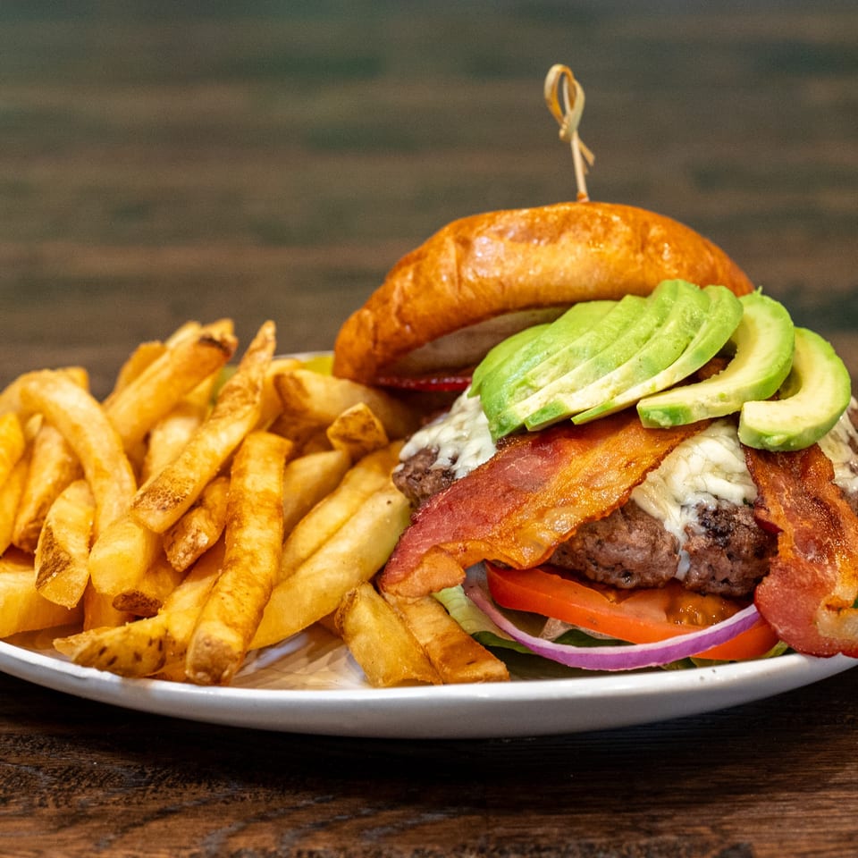 A Brunchy's Cafe burger with bacon, avocado, and cheese, served with a side of fries.