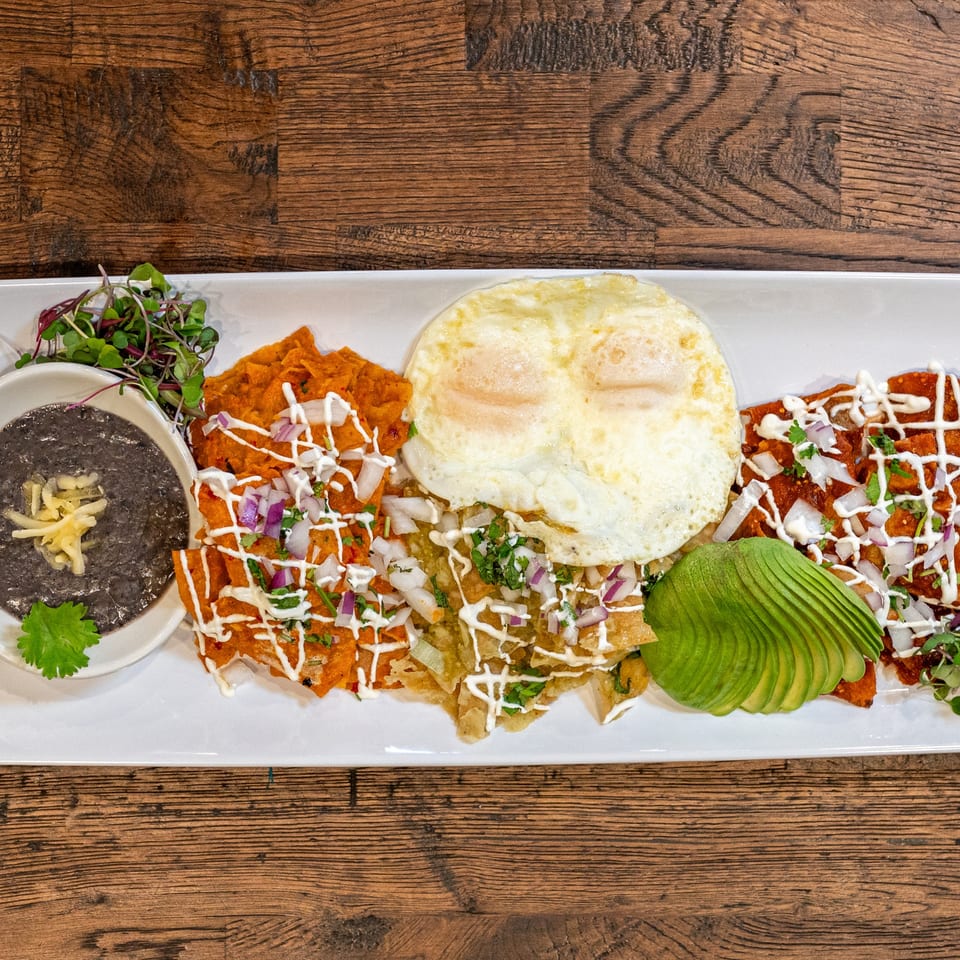 A Brunchy's Cafe chilaquiles plate with black beans, two fried eggs, and sliced avocado.