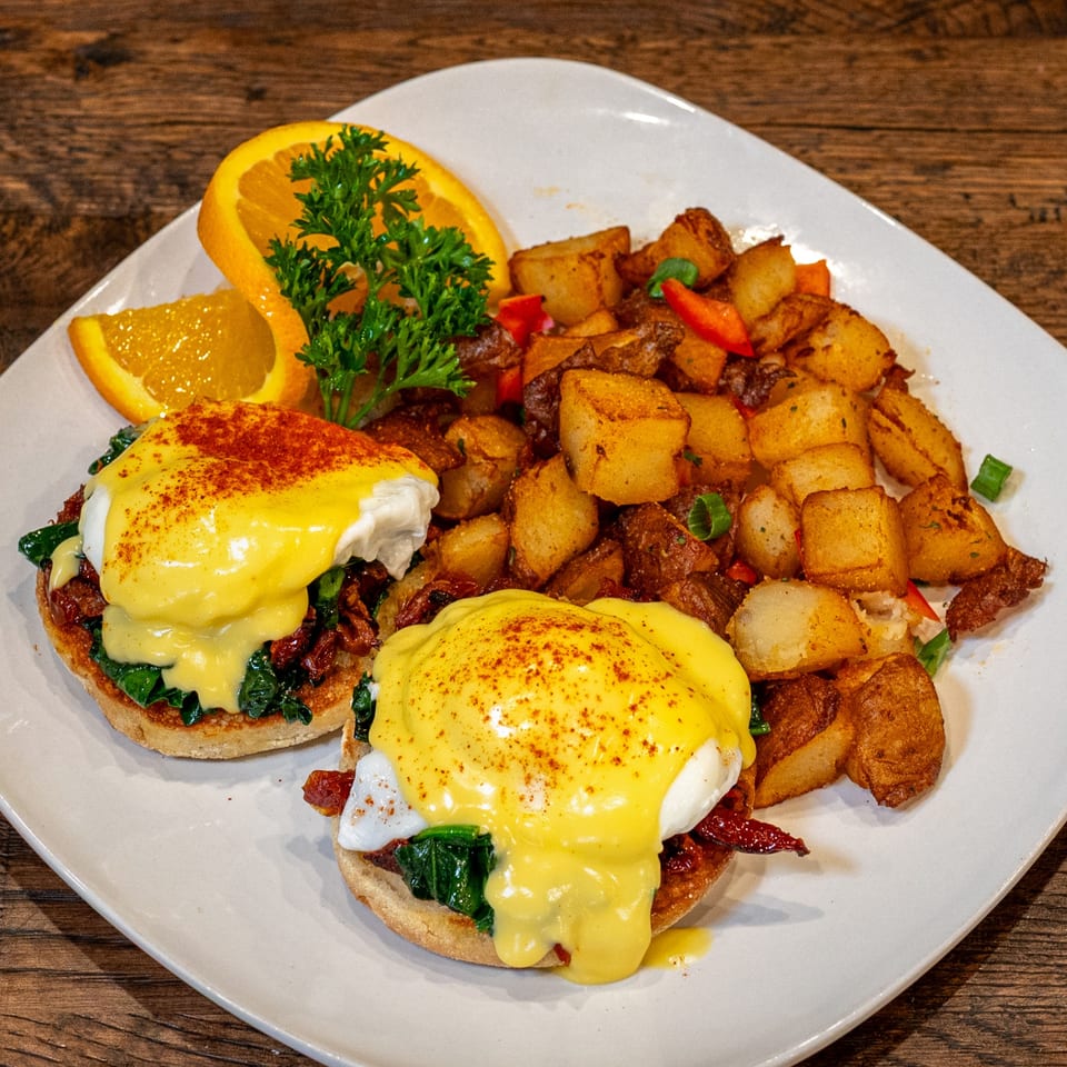 Brunchy's Cafe Eggs Benedict with hollandaise, home fries, and orange slices on a white plate.