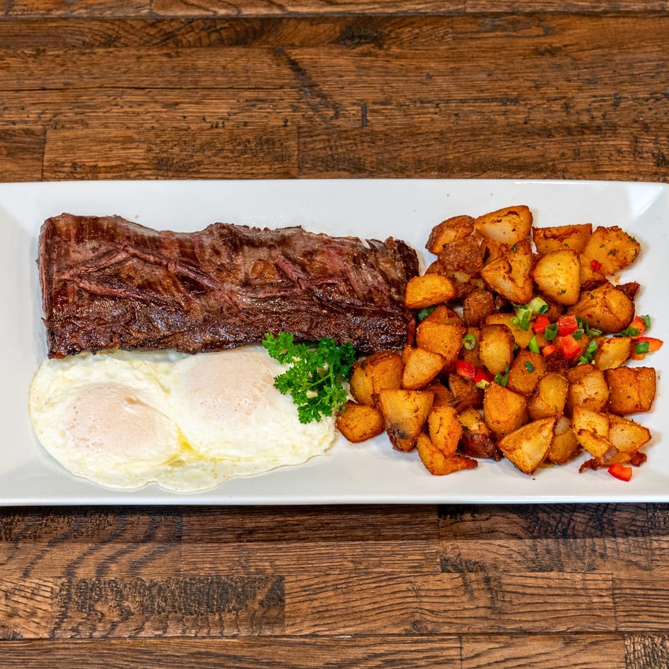 Brunchy's Cafe steak and eggs breakfast with home fries, garnished with parsley on a white plate.